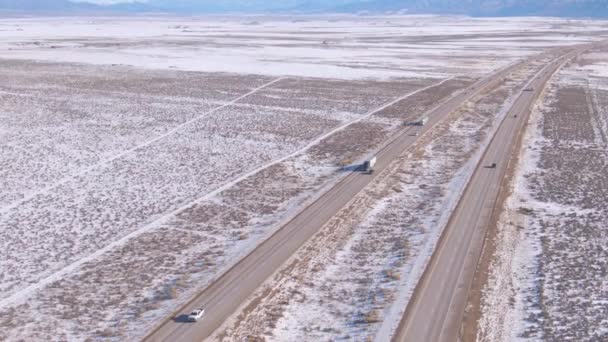 当两辆白色卡车载着货物穿过白雪覆盖的沙漠时，飞机在高速公路上方飞驰 — 图库视频影像