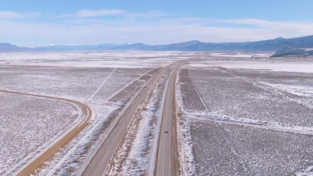 AERIAL: Volando a lo largo de una carretera de asfalto que conduce vehículos a través del desierto nevado — Vídeos de Stock