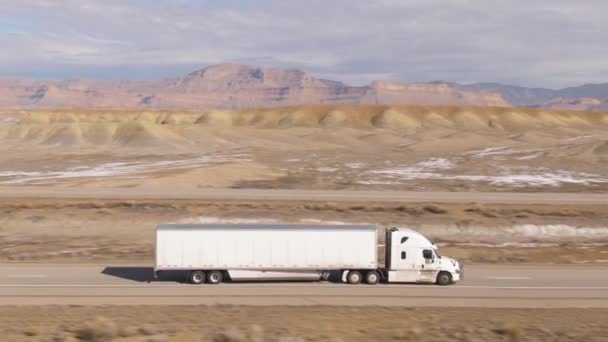 AERIAL:砂漠を横断する高速道路沿いのセミトレーラートラックの速度 — ストック動画