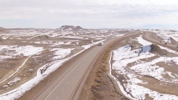 Volando por encima de una carretera mientras un camión blanco cruza el desierto nevado en Utah . — Vídeos de Stock