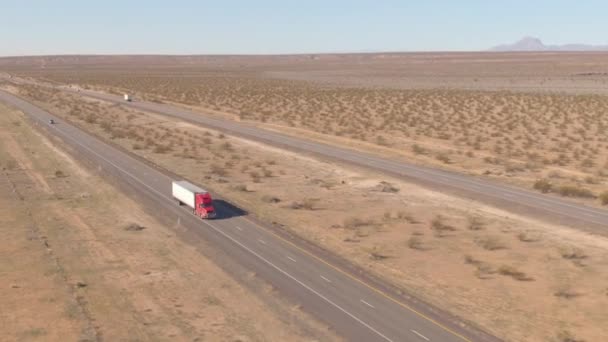 AERIAL: Camión de carga rojo transporta un contenedor pesado a través del paisaje estéril. — Vídeos de Stock