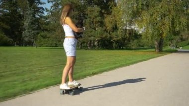 Tanımlanamayan kadın kaykay sürerken köpeğini tutuyor.