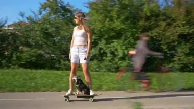 Mutlu kız ve minyatür pinscher havalı bir e-sörf tahtasıyla parkta geziyorlar..
