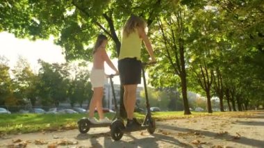 Genç kadınlar elektrikli scooter sürerken kahkahalarla gülüyorlar..