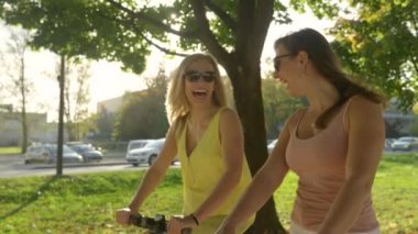 Neşeli bayan arkadaşlar elektrikli scooter sürerken konuşur ve gülerler..