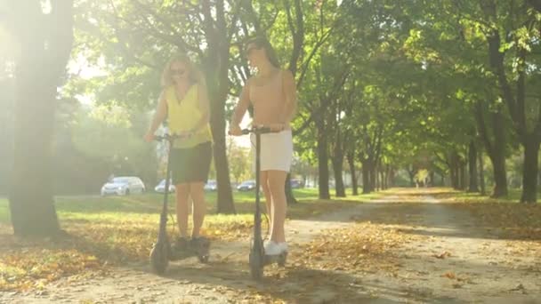 太陽のフレア:女の子は公園の周りのe-scootersに乗ることによって晴れた秋の日を楽しむ. — ストック動画