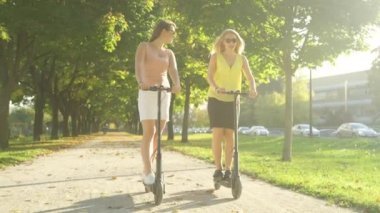 Güneşli bir günde elektrikli scooter kullanan kadınların üzerinde altın güneş ışınları parlıyor.