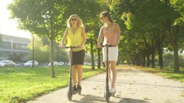 Parkta e-scooter sürerken gülümseyen ve konuşan iki kadın.