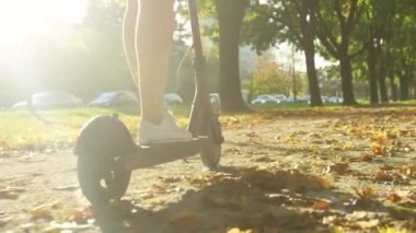 Genç milenyum kadını, güneş parkında elektrikli scooter kullanıyor.