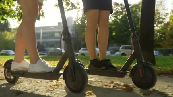 FLARE DE LA LENTE: Foto cinematográfica de mujeres en faldas montando e-scooters en un día soleado — Vídeos de Stock