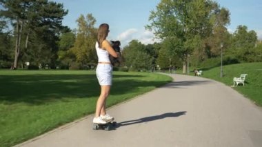 Neşeli kadın e-longboard sürerken köpeğini tutar ve öper.