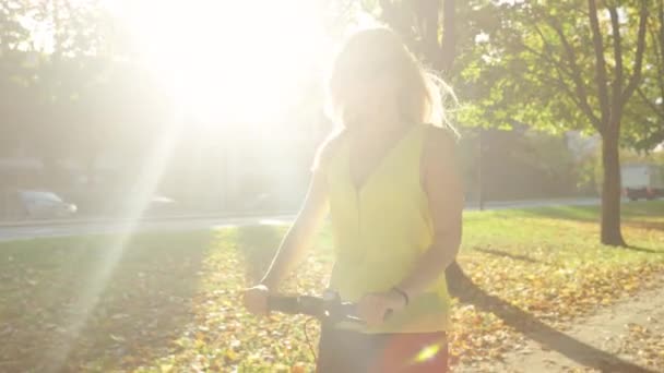 CERRAR: Hermosa chica rubia monta un scooter eléctrico alrededor del parque escénico — Vídeos de Stock