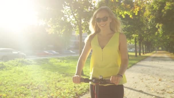 Ritratto: Bella donna gode di un giro in scooter elettrico lungo un viale illuminato dal sole. — Video Stock