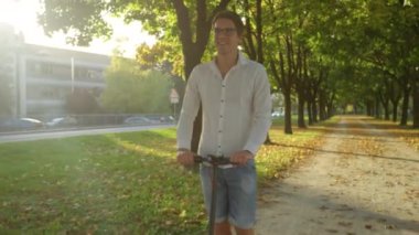 Genç beyaz bir adam elektrikli scooterla manzaralı bir caddede ilerliyor..