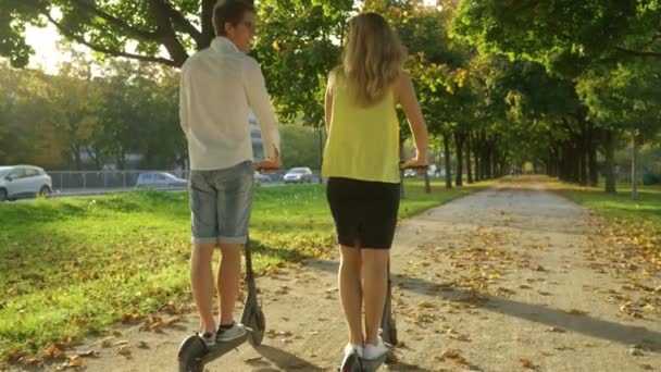 LENS FLARE: bekymmerslösa par rider elektriska skotrar på en solig höstdag. — Stockvideo