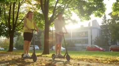 Genç çift, güneşli caddede e-scooter sürerken konuşuyor..
