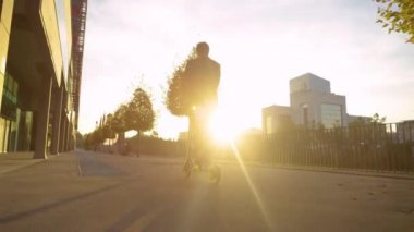 Tanınmayan takım elbiseli adam gün doğumunda işe elektrikli scooterla gidiyor.