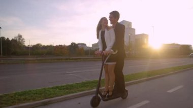 Resmi kıyafetli genç çift gün batımında elektrikli scooter kullanıyor..