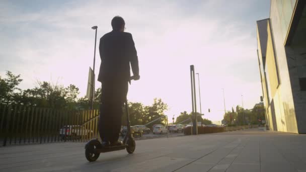 LÅG ANGLE: Golden solstrålar skina på affärsman pendling till jobbet på e-scooter. — Stockvideo