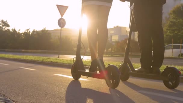 CLOSE UP: Gouden zonnestralen schijnen op twee collega 's rijden elektrische scooters. — Stockvideo