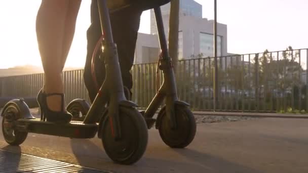 LENS FLARE Empresario y su compañera de trabajo montan scooters eléctricos al atardecer — Vídeo de stock