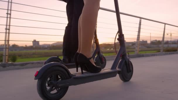 FECHAR UP: Feixes de sol quentes brilham em homens de negócios e mulheres andando de scooters ao pôr do sol — Vídeo de Stock