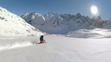 Kadın snowboardcu, güneşli bir günde el değmemiş dağı oyuyor..