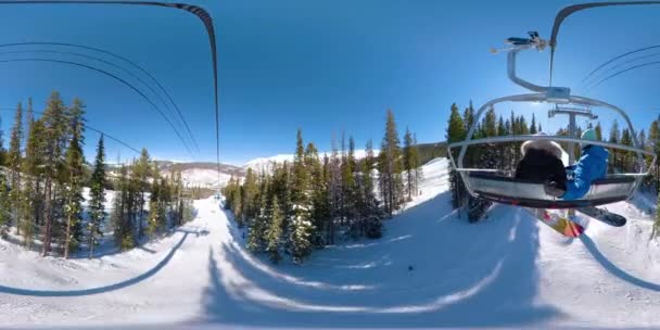 360 VR: Άνδρας και γυναίκα οδηγούν τον ανελκυστήρα καρέκλα κατά τη διάρκεια ενός ταξιδιού snowboarding στο Κολοράντο — Αρχείο Βίντεο