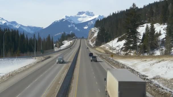 AERIAL: Scenic shot of traffic moving along autoway with view of snowy mountains — Vídeo de Stock