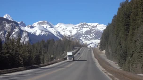 Fotografía cinematográfica de camiones y coches que conducen por un camino pintoresco bajo montañas nevadas — Vídeos de Stock