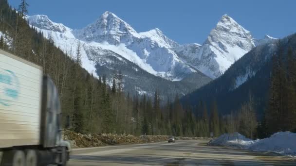 Traffico si muove lungo una strada di campagna sotto le montagne innevate in Alberta. — Video Stock