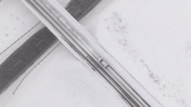 ARRIBA: Volando sobre el coche conduciendo a lo largo de un puente nevado cruzando una carretera vacía. — Vídeos de Stock
