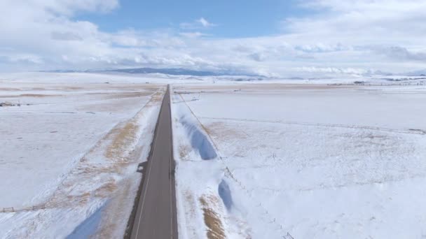 AERIAL: Vliegen langs lege asfaltweg die besneeuwde vlakten kruist in Montana — Stockvideo