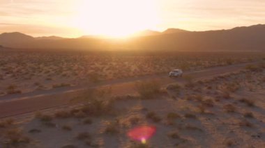 Nevada çölünü geçen SUV üzerinde parlayan altın güneş ışınlarının sinematik görüntüsü..