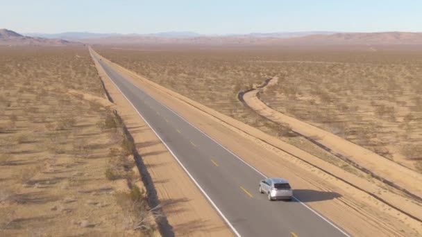 Volando detrás de un coche plateado mientras conduce por una carretera que cruza el desierto — Vídeo de stock