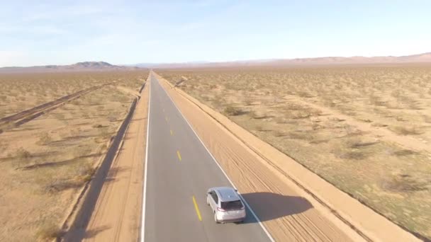 AERIAL: Hinter einem silberfarbenen SUV durch die zerklüftete Mojave-Wüste. — Stockvideo