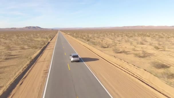 DRONE : Un paysage aride entoure un 4x4 argenté qui descend une autoroute vide. — Video