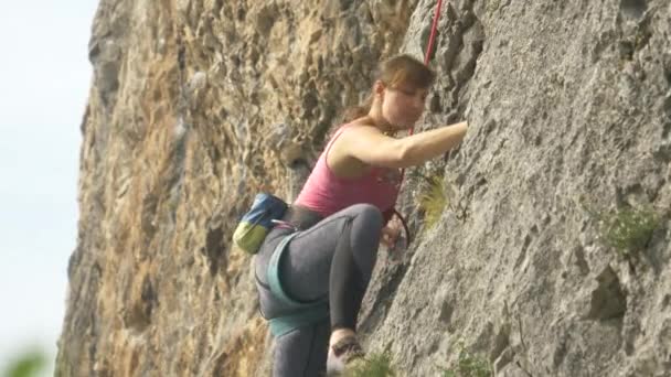 Fiatal női sziklamászó mászik egy hatalmas sziklán egy napsütéses napon.. — Stock videók