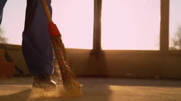 LOW ANGLE: Contractor sweeping the dirty floor with a straw broom at sunset. — Stock Video