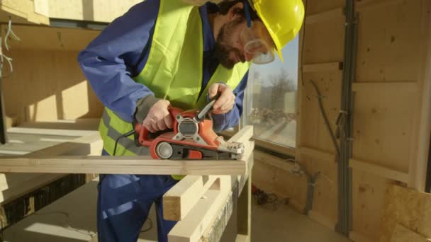 CLOSE UP: Bauarbeiter mit Bart schleift auf einer Baustelle einen Holzbalken — Stockvideo