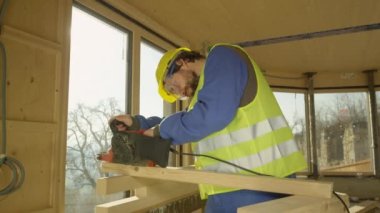 Prefabrik bir evde çalışan genç adam zımpara makinesiyle tahta cilalıyor.