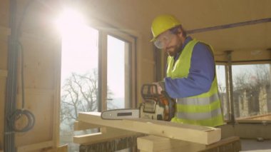 Genç müteahhit, uzun bir kirişi ikiye bölmek için elektrikli testere kullanıyor..