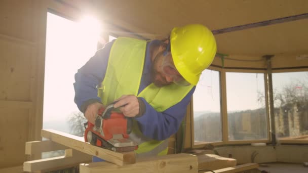 GESCHLOSSEN: Bärtiger Bauunternehmer glättet mit Schleifer fleißig einen Holzbalken. — Stockvideo