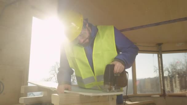 LENS FLARE: Bouwer aan het werk in een CLT-huis snijdt een gipsplaten wandpaneel met decoupeerzaag. — Stockvideo