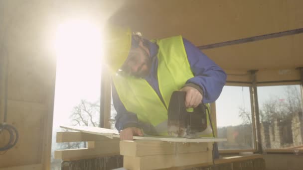 LENS FLARE: Robotnik budujący dom z drewna liściastego przycina ścianę gipsową. — Wideo stockowe