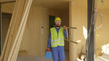 İşçi işe geliyor, alet çantasını ve merdivenini odanın diğer tarafına taşıyor..