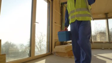 Mavi tulumlu inşaatçı güneşli bir akşamda prefabrik evden ayrılıyor..