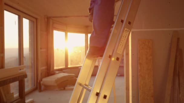 LENS FLARE : Le constructeur en salopette bleue descend une échelle en aluminium au coucher du soleil. — Video