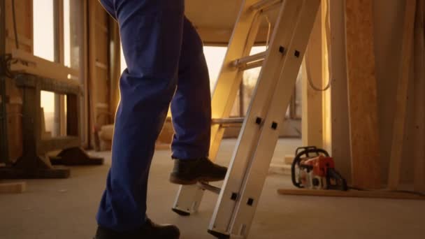 Mavi tulumlu inşaatçı gün batımında alüminyum bir merdivene tırmanır.. — Stok video