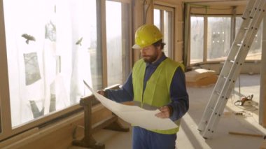 Proje yöneticisi planlara ve inşaat halindeki bir eve bakıyor..